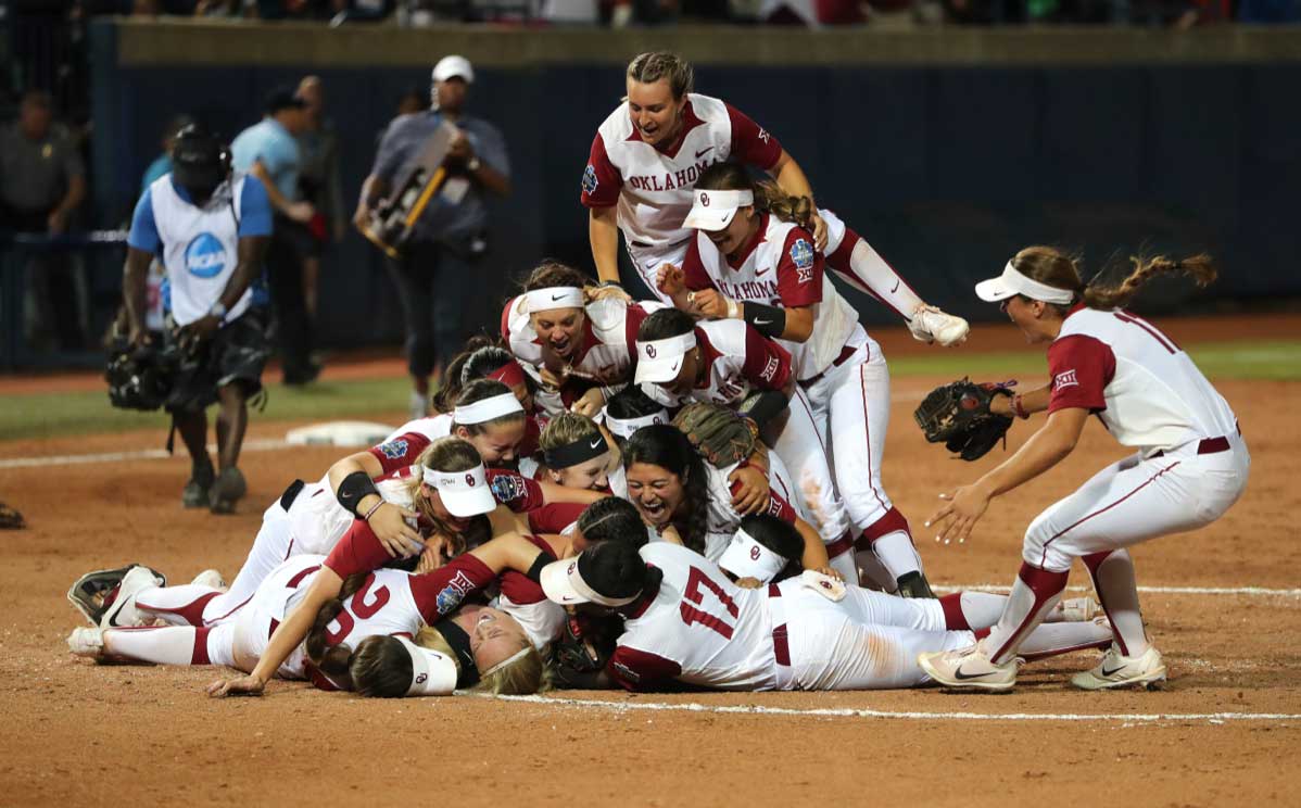 Fifteen softball athletes are forming a dog pile a the conclusion of a win