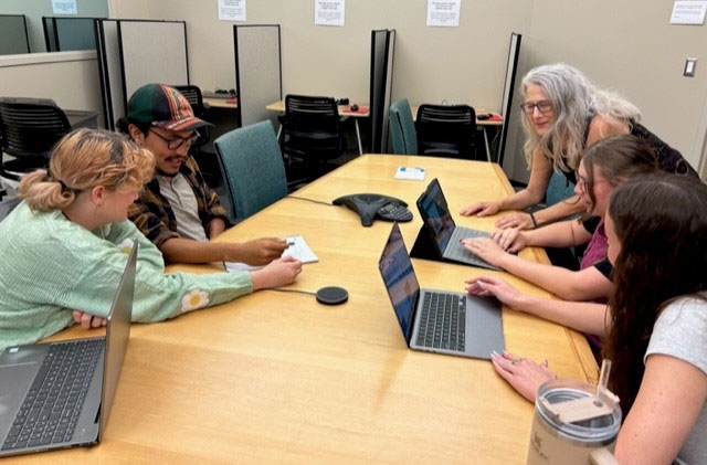 Medical Anthropology Students and Faculty Member Sitting at Table with Computers, in Discussion with One Another