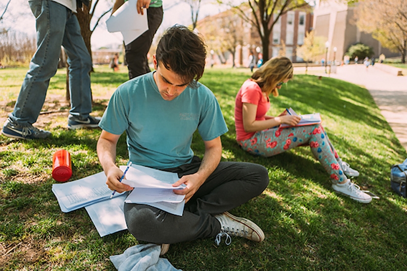 OU students sitting on a grassy knoll in front of Bizzell Memorial Library looking at their notes.