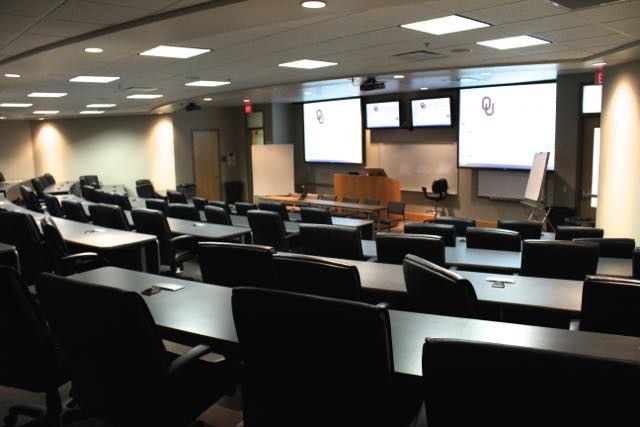 A large classroom space with two large, front facing monitors and a lectern