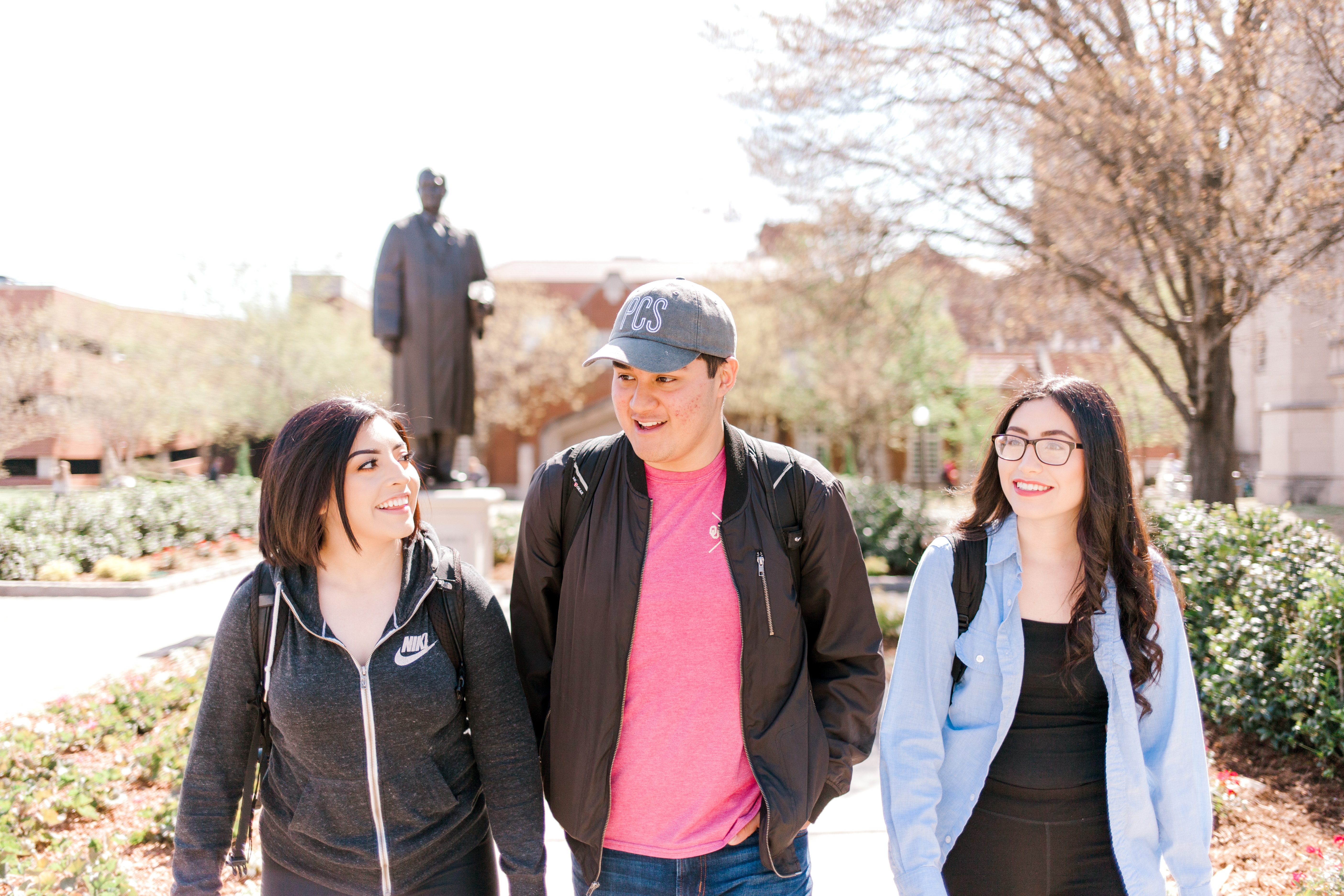 Three students walking on campus with David L. Boren statue in background