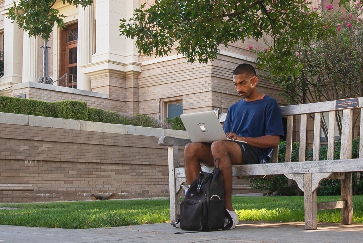 A student sitting on bench with laptop. 