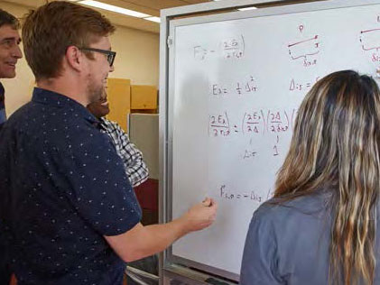 Students working with professor at white board. 
