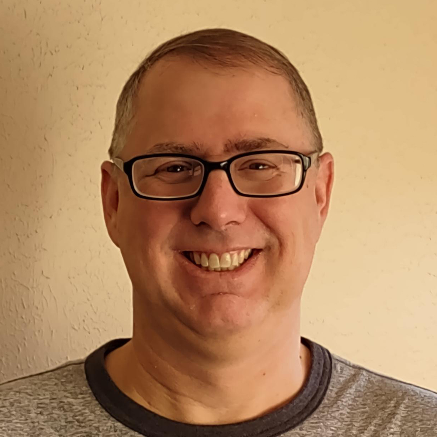 Man in a gray t-shirt with glasses smiling at the camera