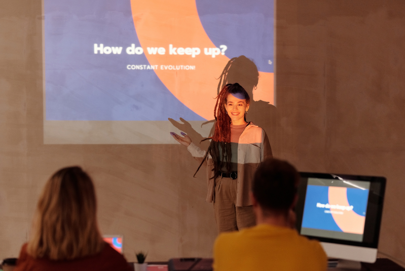 A woman with long hair standing in front of a power point presentation looking at the audience