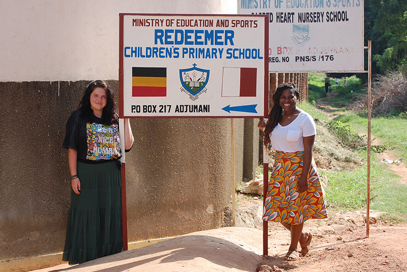 two students standing in front of a school sign in Uganda