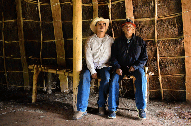 Two men sitting in a teepee, looking at the camera.
