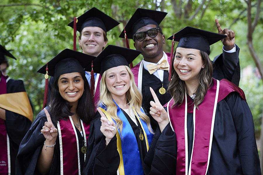 A group of graduates in their regalia giving the 'one OU' sign.