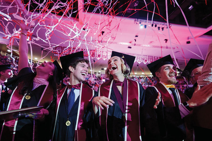 Students in regalia, with streamers falling and bright lighting in the background.
