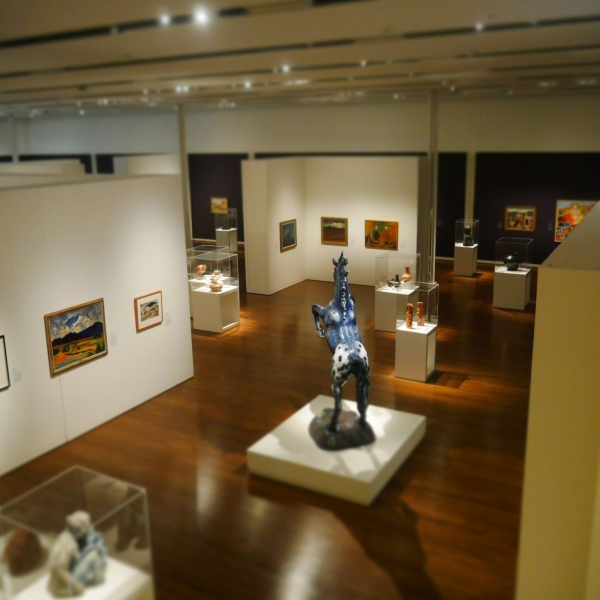Art gallery with paintings, pottery, and a large statue of a horse.
