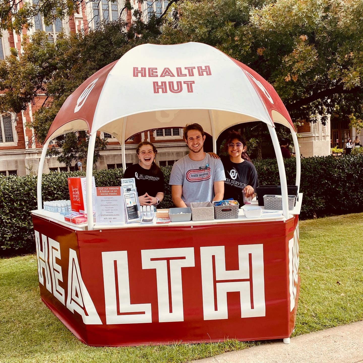 three students smiling at health hut outside near the library