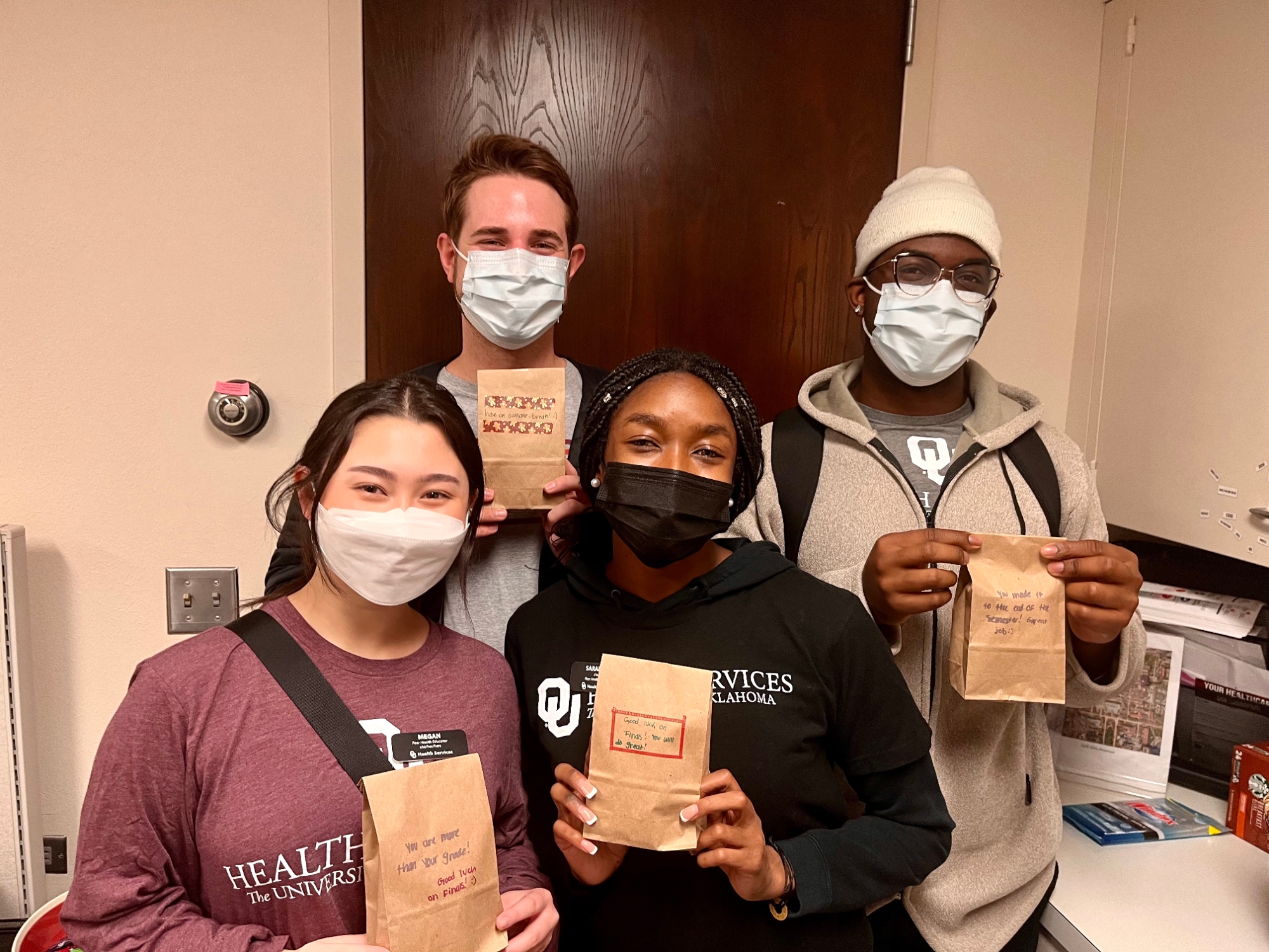 five students smiling while holding goodie bags to distribute during finals week