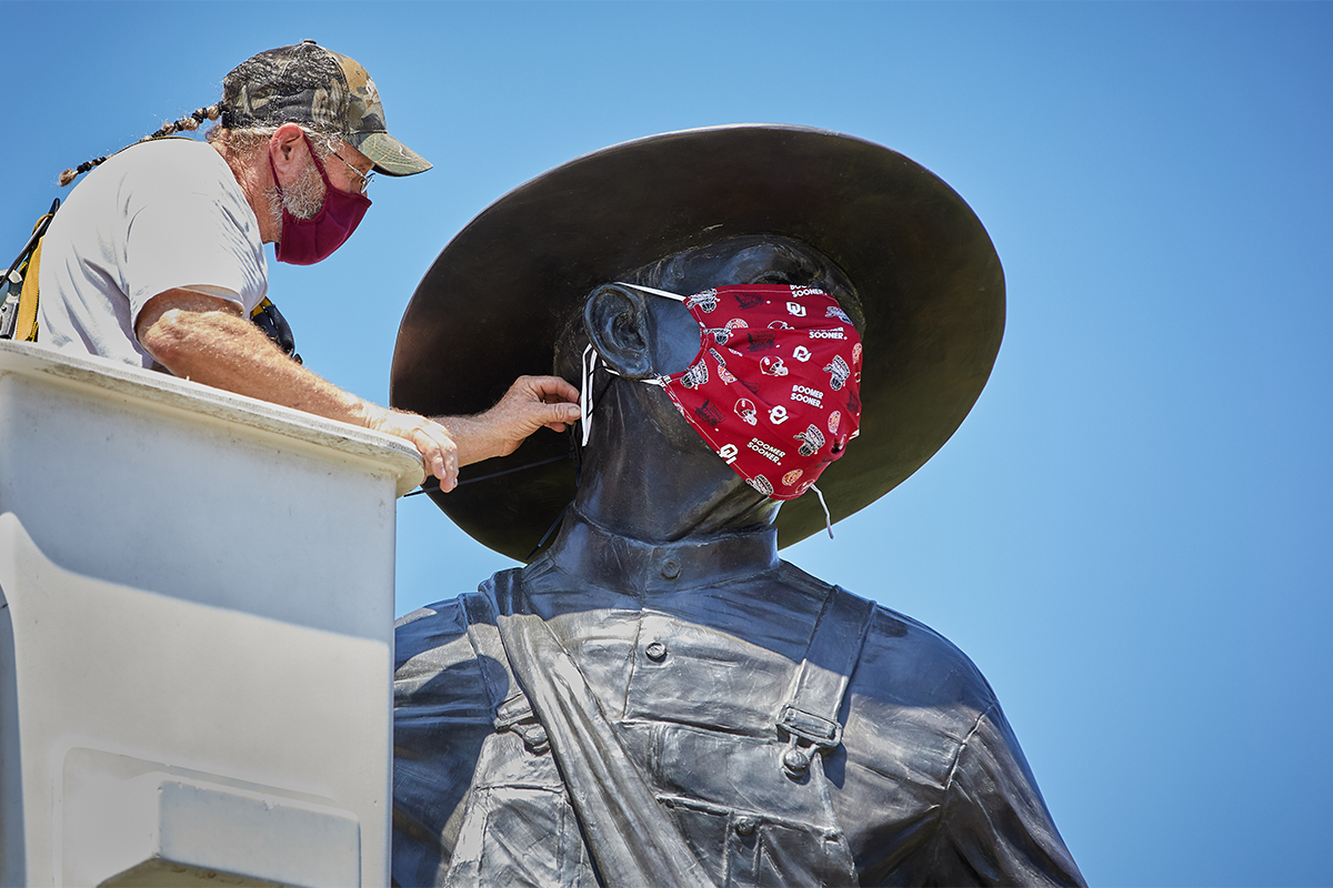 staff member places a cotton face mask on the Sower statue