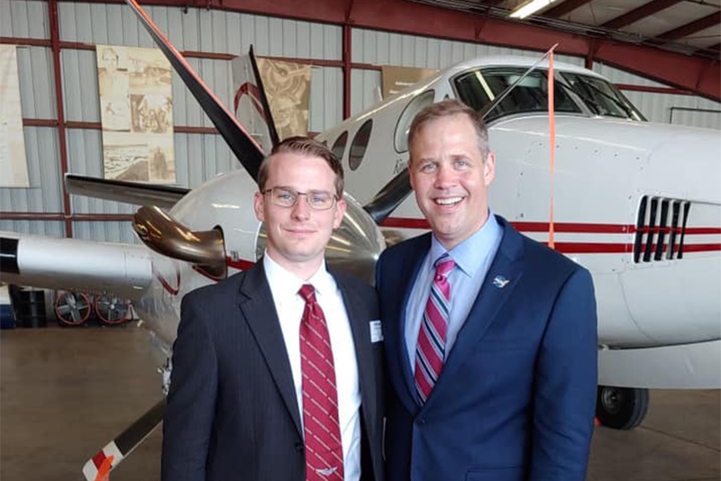 Lance Lamkin poses for photo in hanger with Jim Bridenstine, airplane parked behind them