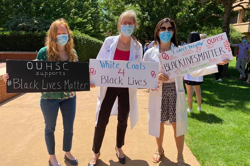 Three women hold signs at OU HSC Black Lives Matter Event: "OUHSC Supports Black Lives Matter" "White Coats for Black Lives" and "Black Lives Matter"