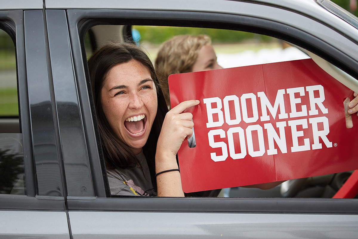 Individual in car holds up "Boomer Sooner!" sign