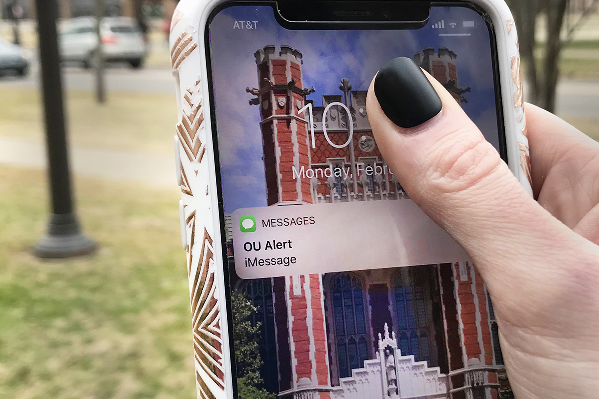 POV shot woman holds up an iPhone with "OU ALERT iMessage" popup on lock screen