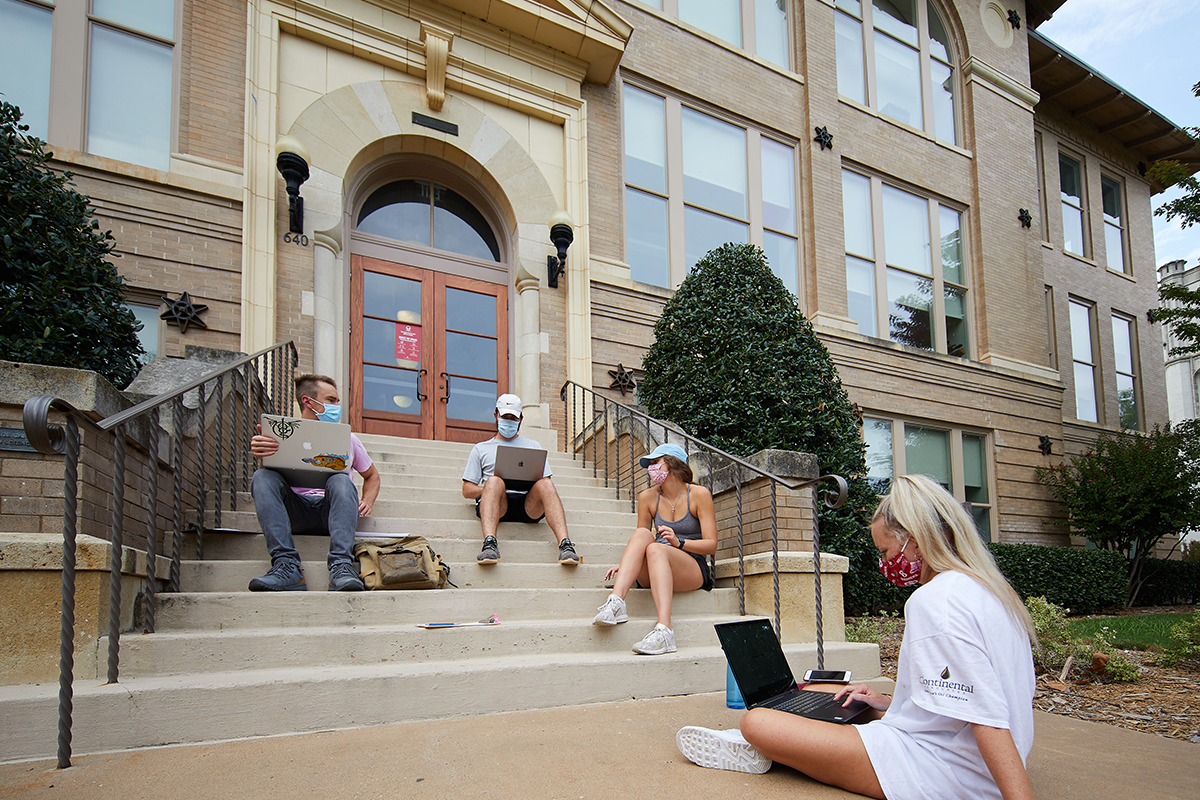 students in masks on the south oval, sitting on steps, studying