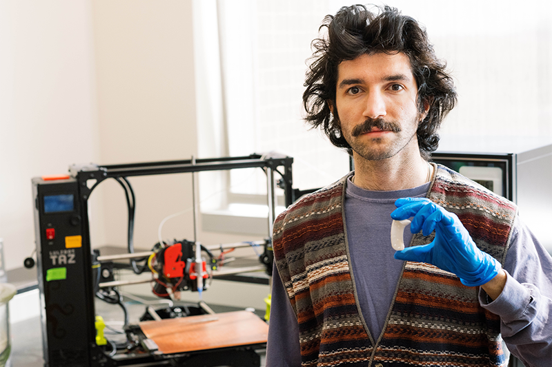 Ali Rassi poses with a 3d printer and printed part