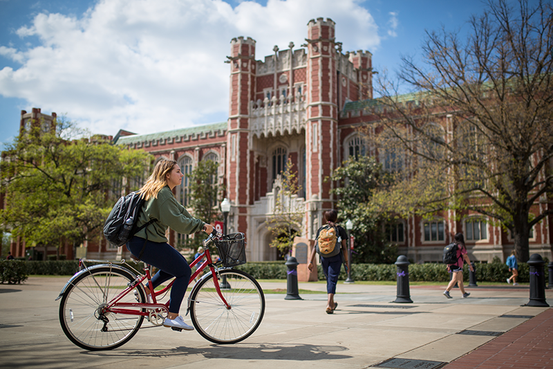 OU Student rides a bike near Bizzell Library in the springtime