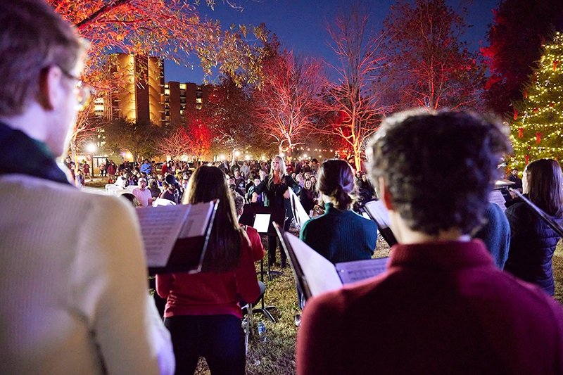 Carolers singing outdoors at the event, photographed from behind