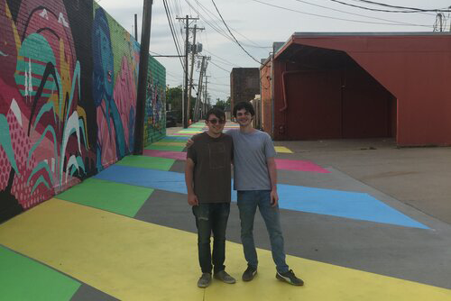 Two IQU interns pose for a photo outside near a mural