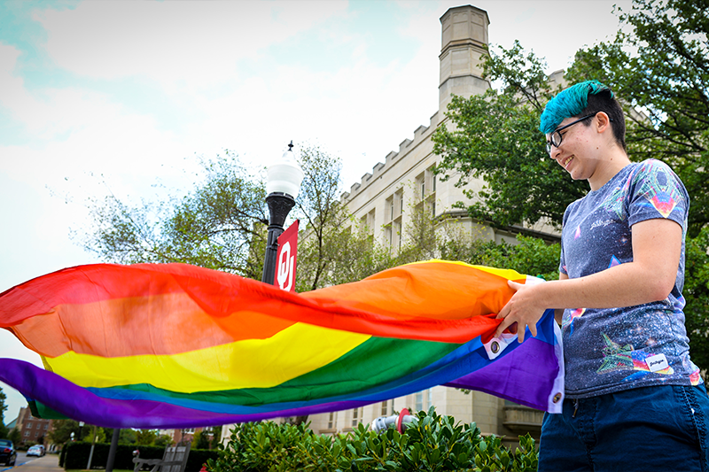 Student unfurls a large rainbow Pride flag near the Old Law building