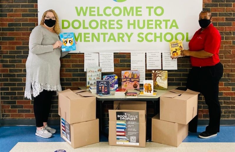 Dolores Huerta Elementary School book drive, two masked people pose for photo alongside several boxes of books