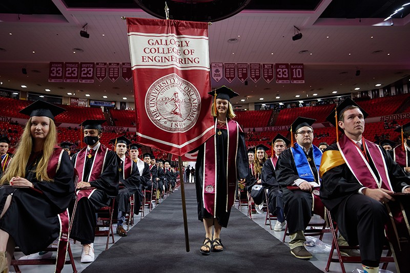 Student walks down the isle holding the flag for College of Engineering