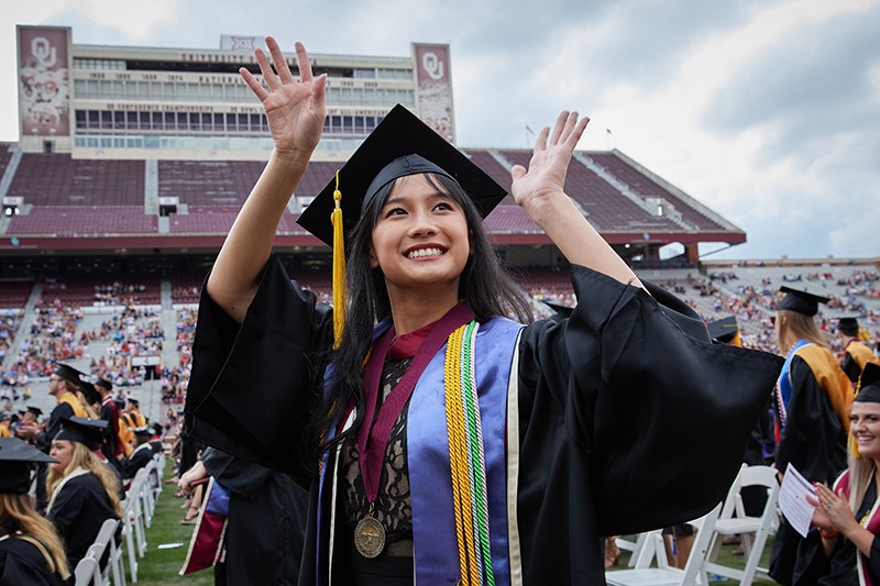 Student waves from the football stadium during ceremony