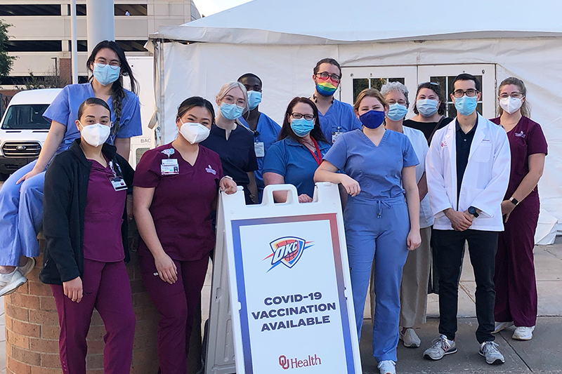 A group of students in scrubs and PPE pose in front of a clinic sign