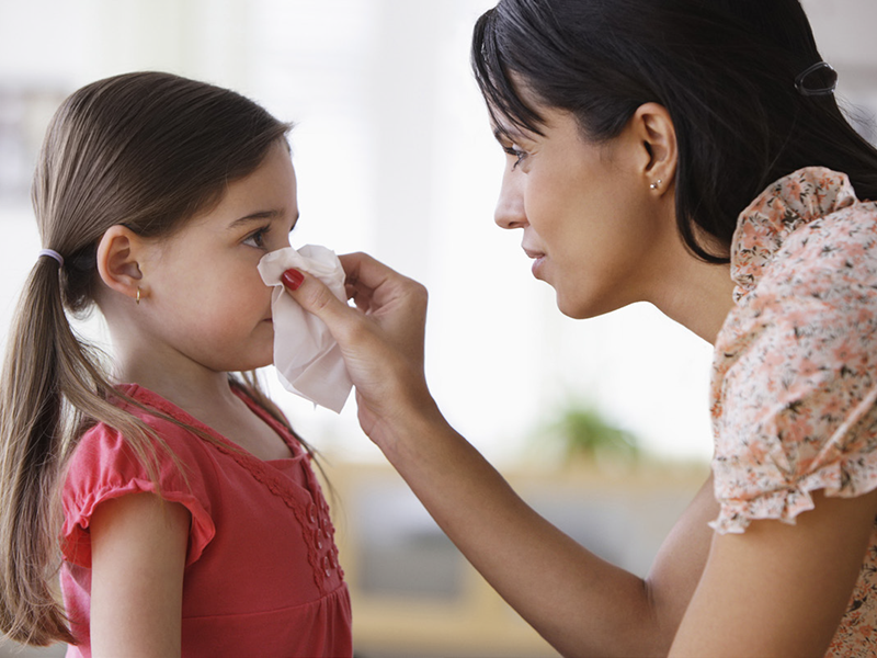 Stock photo woman holds tissue to child's nose