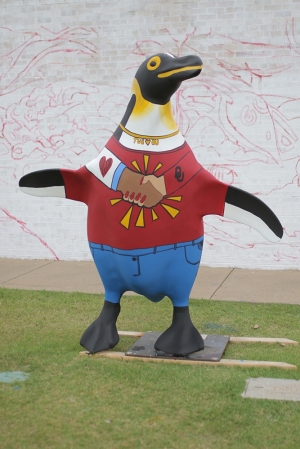 penguin sculpture painted wearing jeans and a tee with a pair of clasped hands across the chest