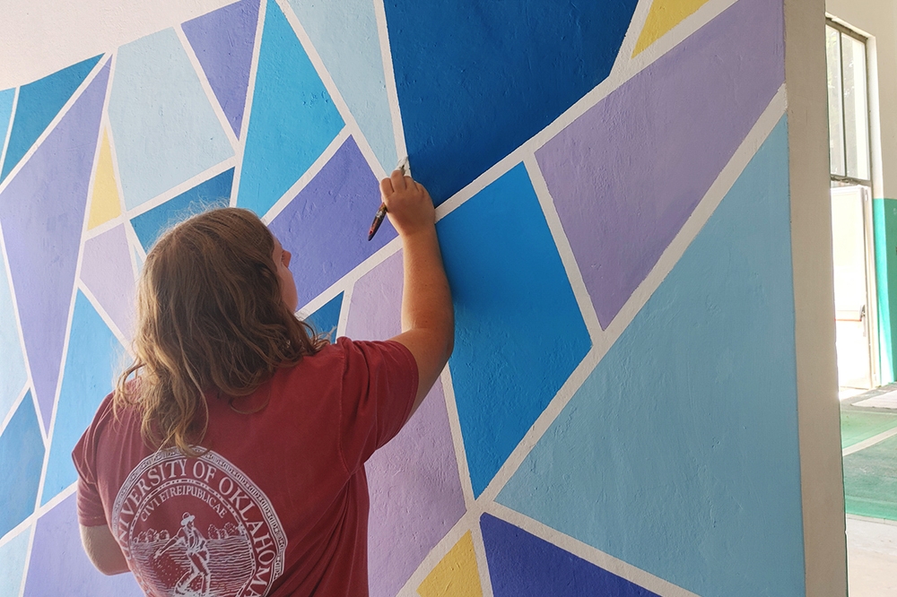 OU student paints a colorful wall in her Seed Sower T-shirt.