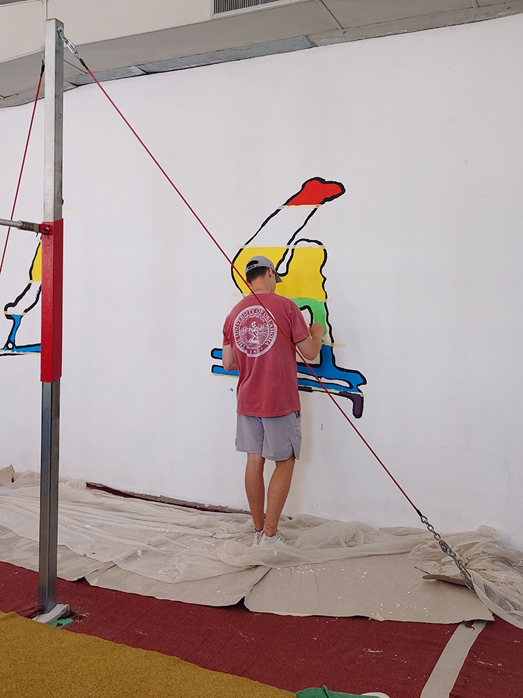 student fills in an outline of a stylized gymnast on a wall mural
