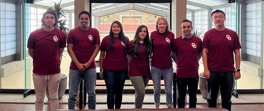 A team of seven students on the Sooners Geothermal Team stand in a glass building.