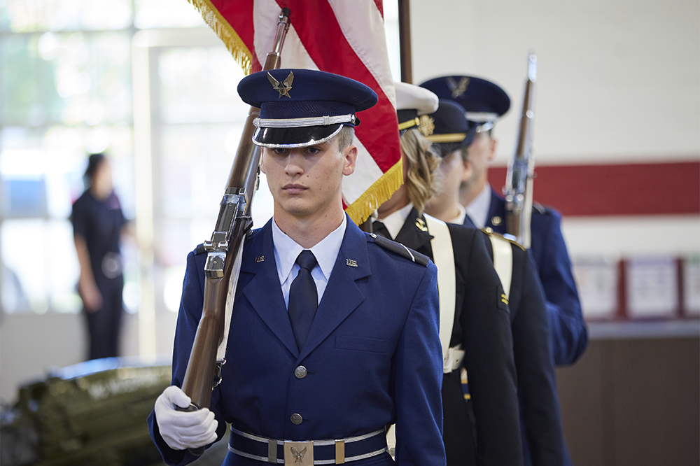 ROTC students march with rifles and flags, in uniform