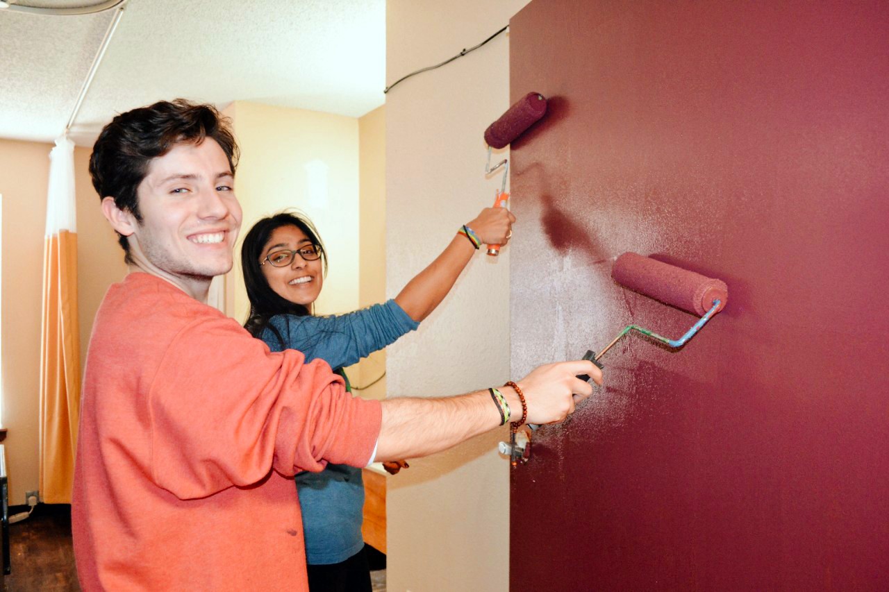 a male and a female student paint a wall with paint rollers