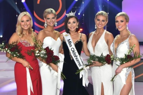 5 women in formal gown pose onstage with flower and pageant ribbonss