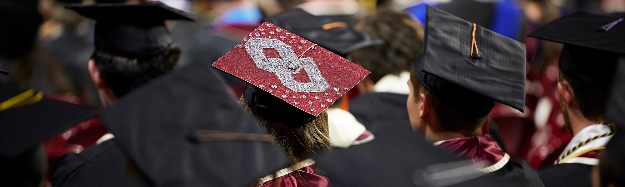 OU students dressed in graduation regalia sitting at a commencement ceremony.