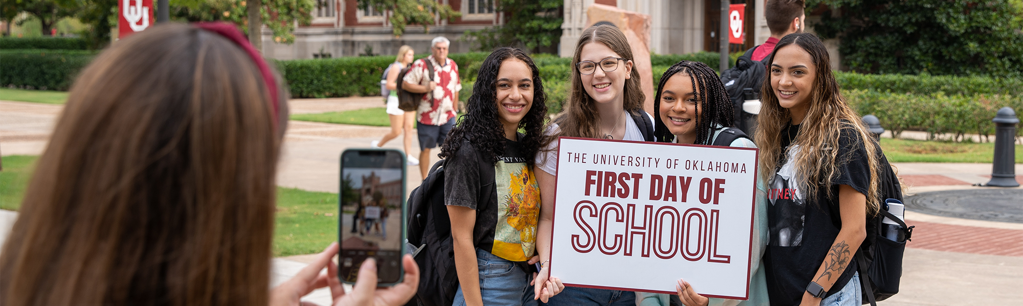 A group of OU students posing for a photo, holding a sign that reads, "The University of Oklahoma First Day of School".