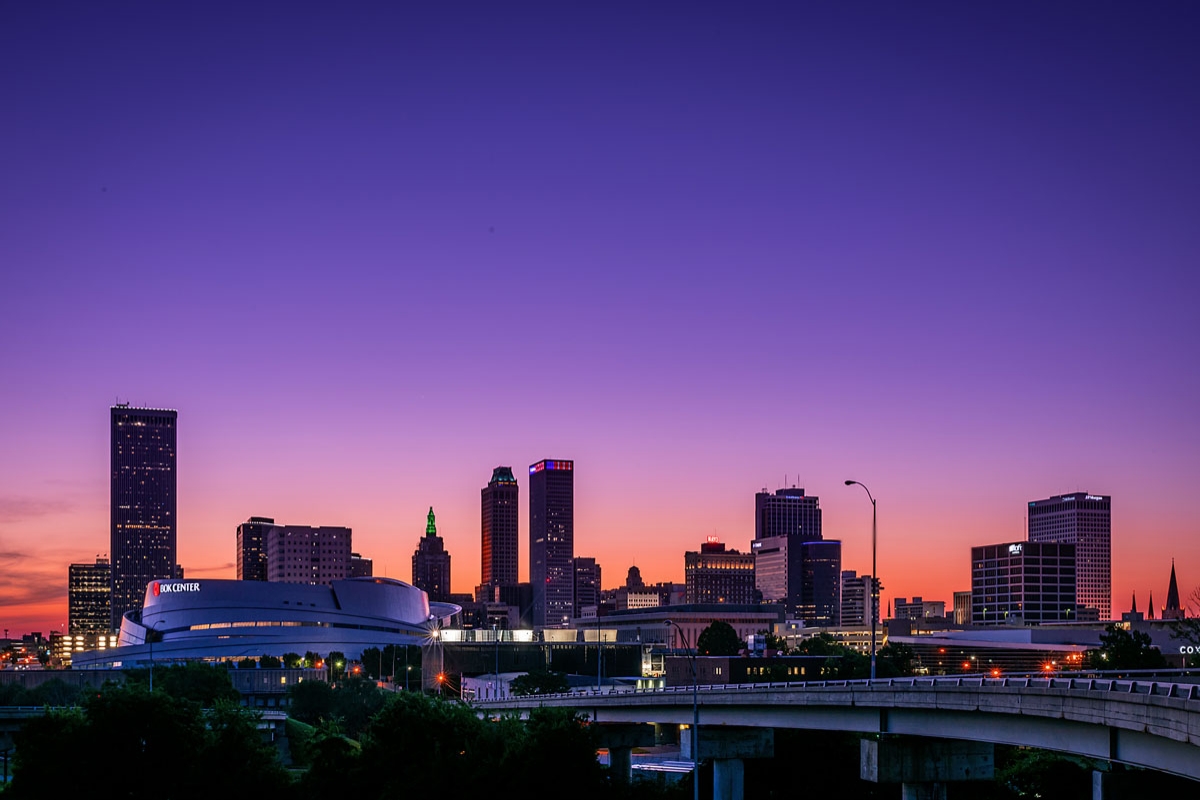 The skyline of Tulsa glitters at twilight, surrounded by a beautiful sunset of purple and orange