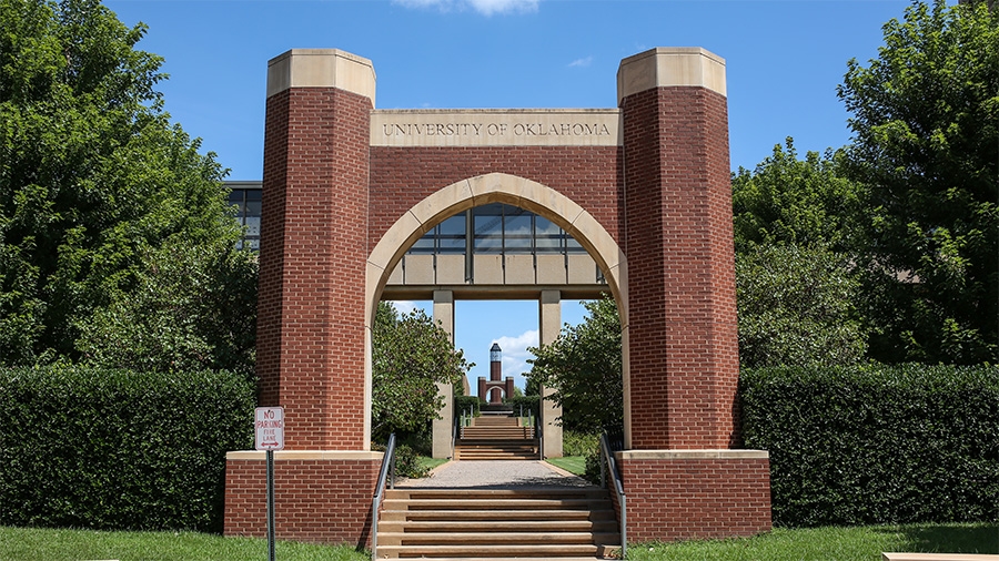 A photo of the Thelma Gaylord arch at OUHSC in Oklahoma City, a red brick arch with "The University of Oklahoma" carved into it. 