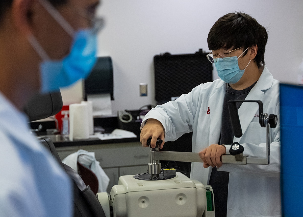 A doctor in a white coat and a surgical mask adjusts a scientific instrument