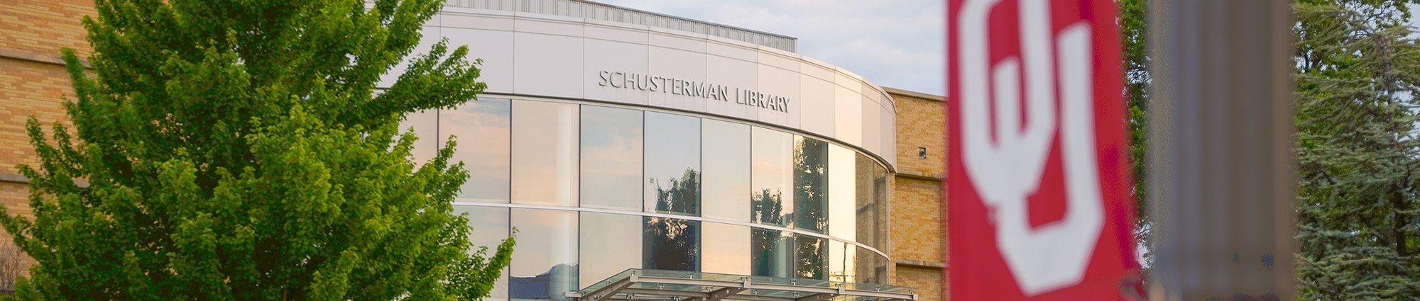 The entrance to the Schusterman Library, with large, picture windows and an OU flag in the foreground