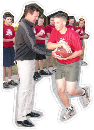 OU football coach handing off football to ROTC student