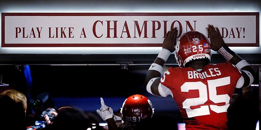 An OU football player touches the "Play like a champion" banner above them.