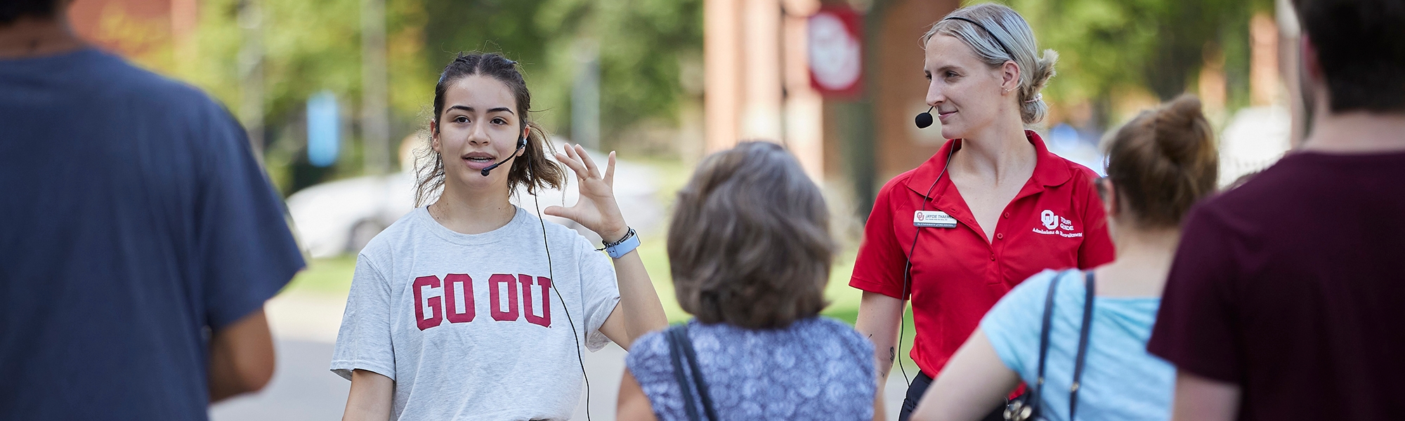 Two OU tour guides walk with a group of visitors on the University of Oklahoma campus.
