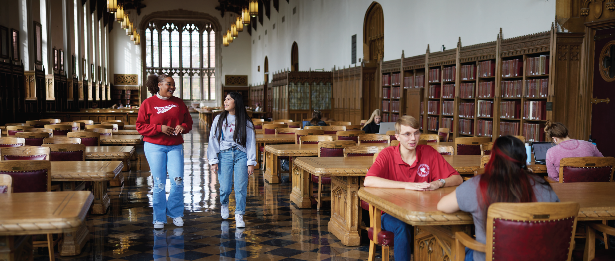 Students sitting at tables and walking in the Great Reading Room in Bizzell Memorial Library.