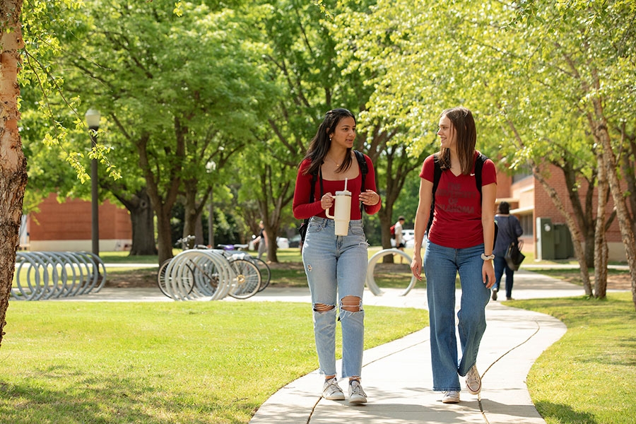 Two students walking surrounded by trees.